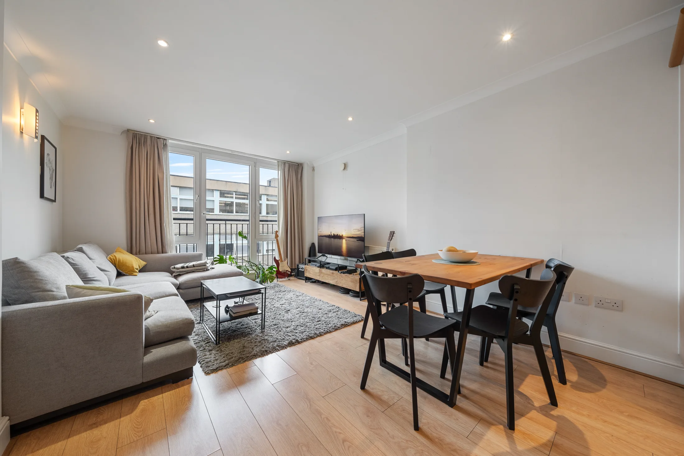 Open-plan reception room with a dining table, sofa and large windows