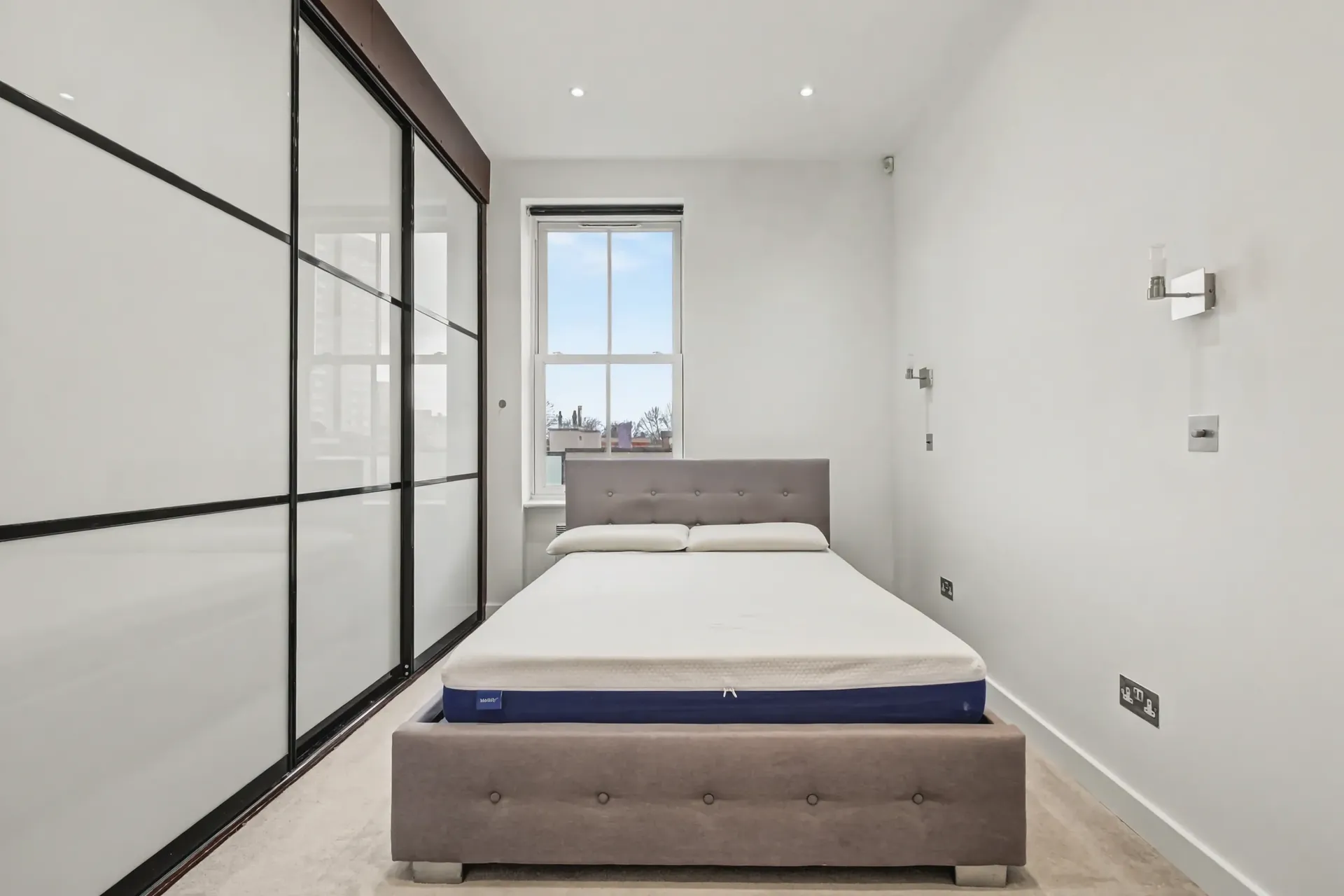 Bedroom with full-height mirrored sliding wardrobes and a sash window