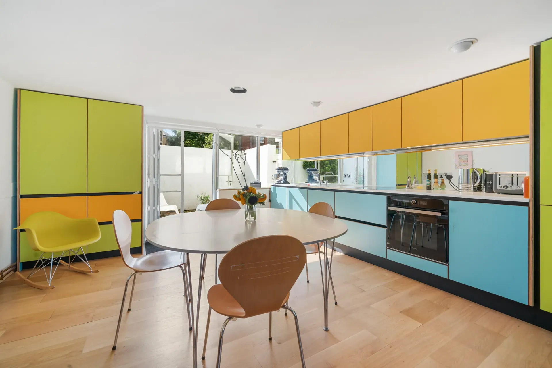 Long fitted kitchen with yellow and blue cabinetry and a dining table