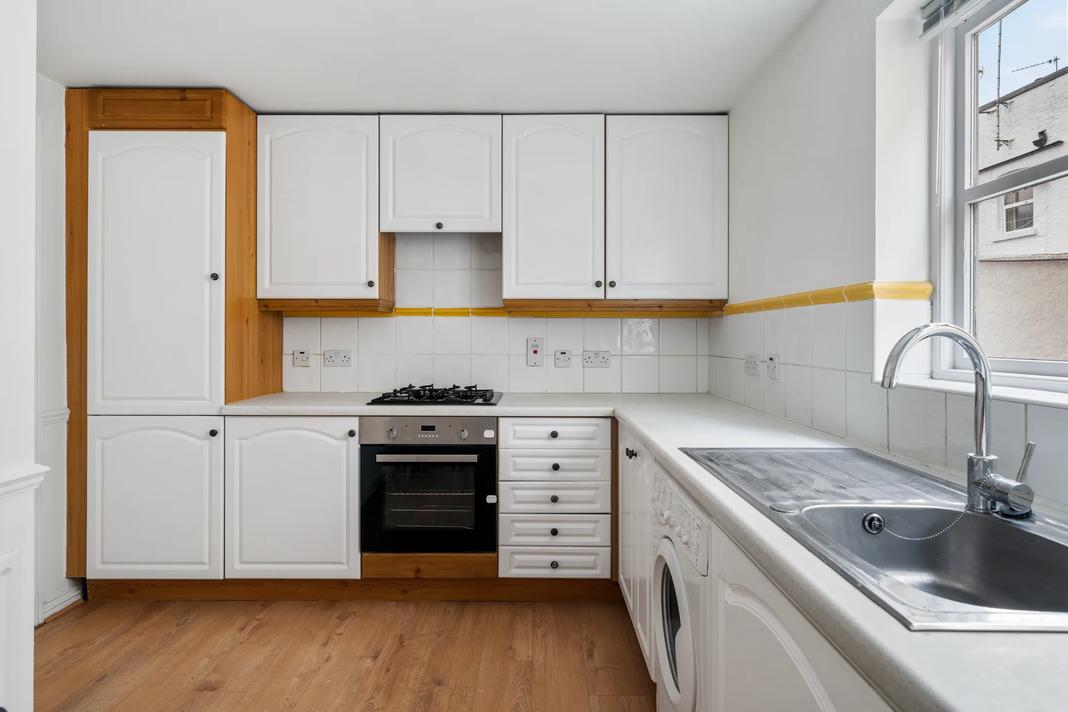 Fitted kitchen with white cabinetry, cooker and stainless sink