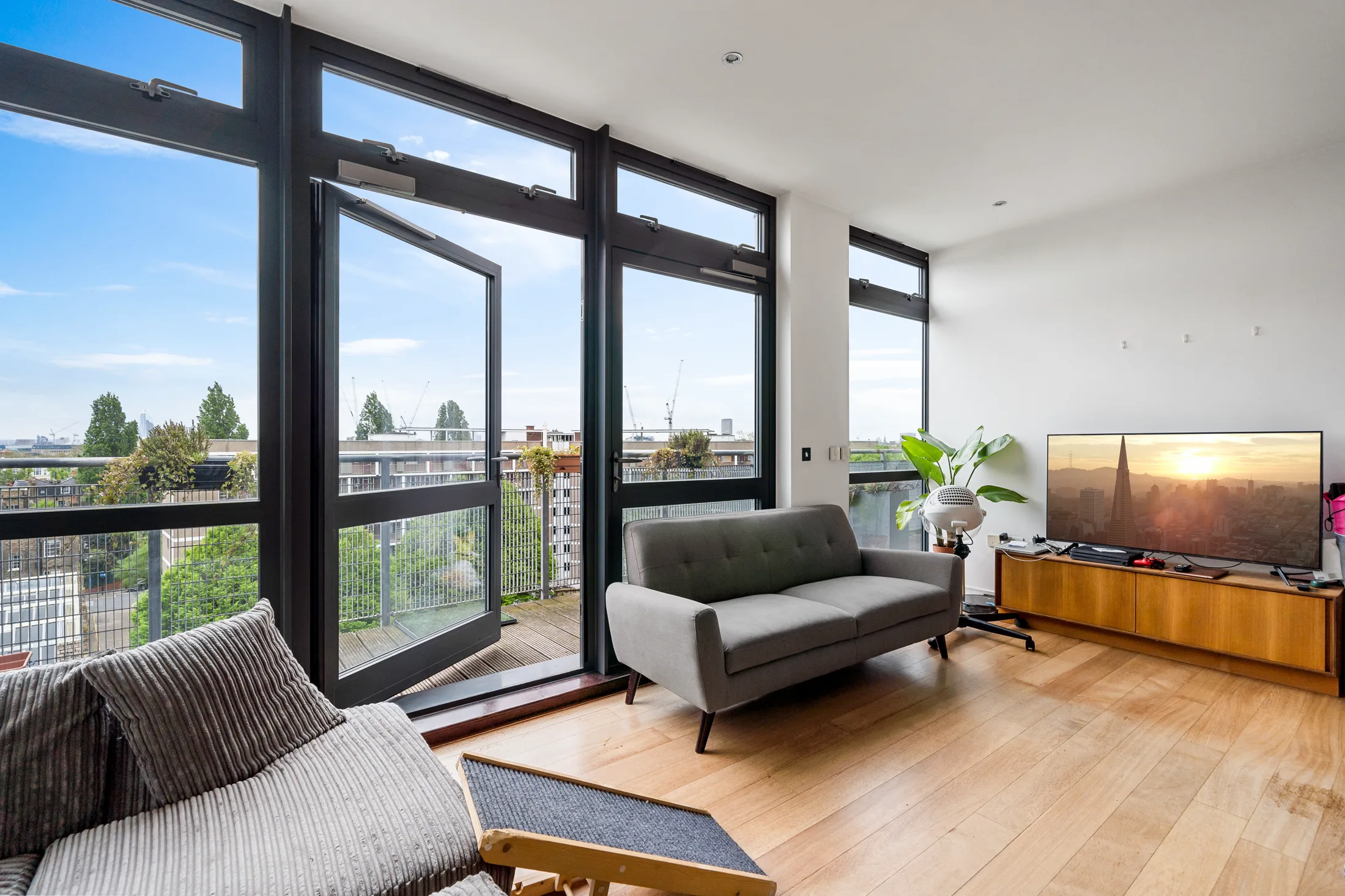 Bright reception room with full-height windows, a balcony and city views