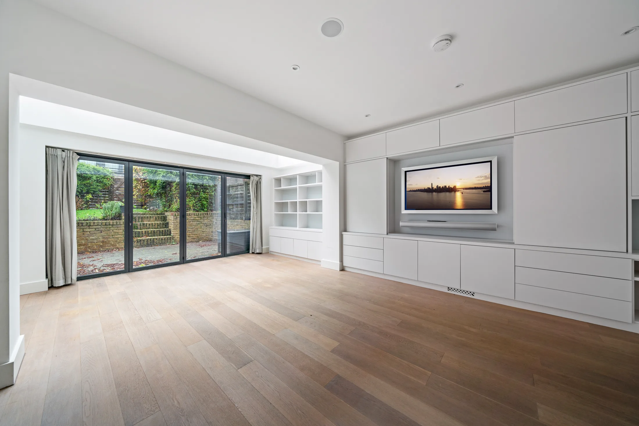 Reception room with timber flooring, fitted wall storage and garden view