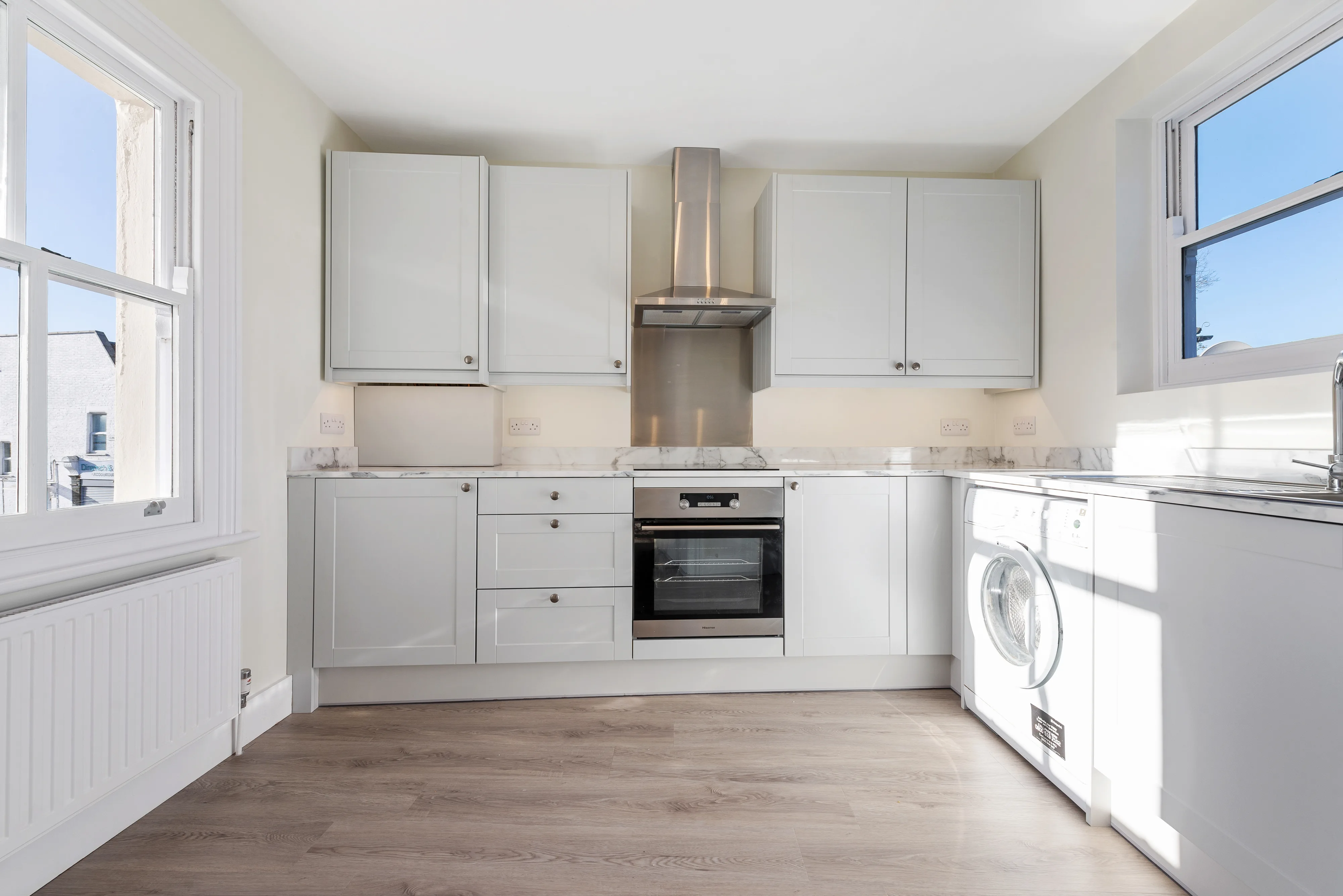 Fitted kitchen with white cabinetry, stainless appliances and two windows
